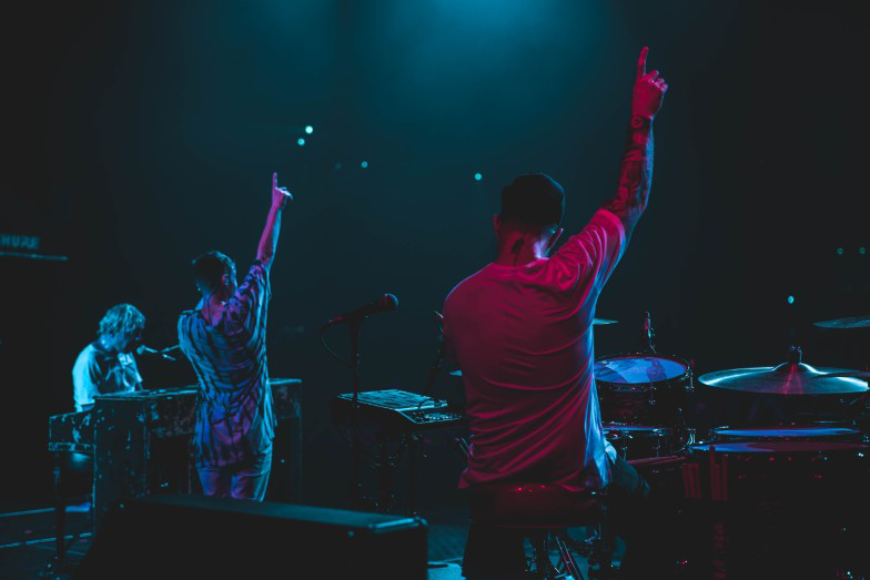 A person playing a piano and 2 artists holding while raising a hand and a finger from the raised arm.