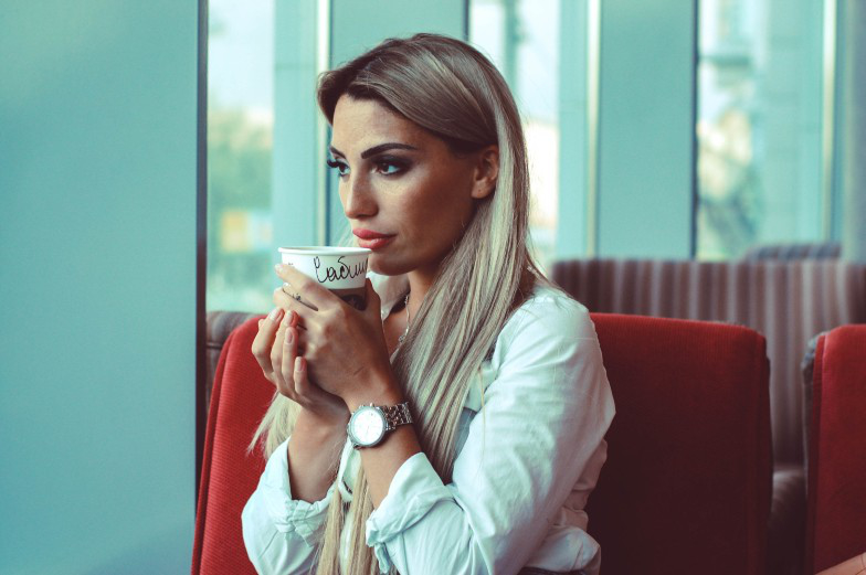 A female sitting near window of a coffee shop, thinking and drinking coffee.